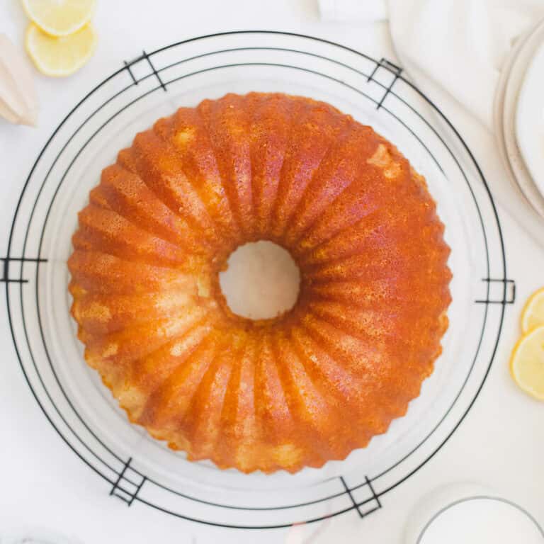 lemon buttermilk bundt cake on a cooling rack garnished with lemons and fresh pink flowers
