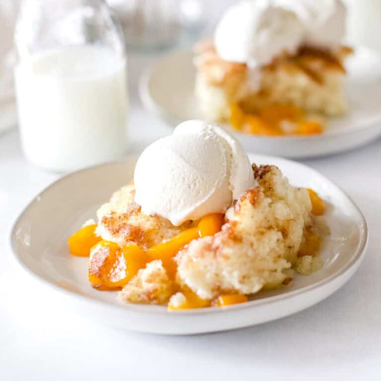 peach cobbler a la mode with vanilla ice cream on white dishes.