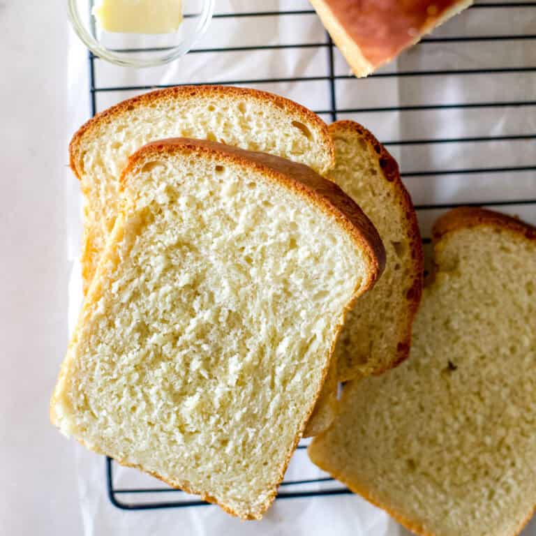 A big loaf of sandwich bread that was baked in a 13-inch pullman pan sliced on a black cooling rack and garnished with a dollop of butter.