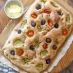 A close up view of sourdough focaccia with tomatoes, olives and artichokes.