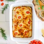 A baked sourdough pizza bread in a white baking dish with tomatoes and mozzarella cheese.