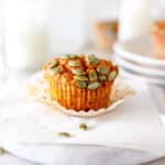 A sourdough discard pumpkin muffin on a white marble platter with the wrapper partially off and several glasses filled with milk in the background.