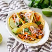 four street tacos on a vintage white platter with limes and cilantro garnishes.
