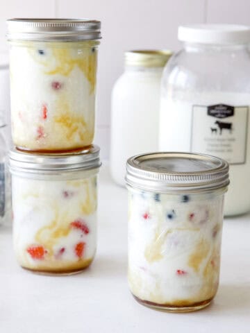 Three yogurt parfaits in mason jars with maple syrup and berries.