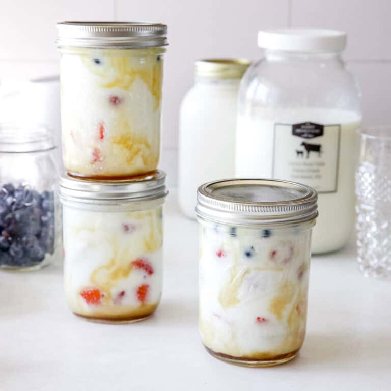 Three yogurt parfaits in mason jars with maple syrup and berries.