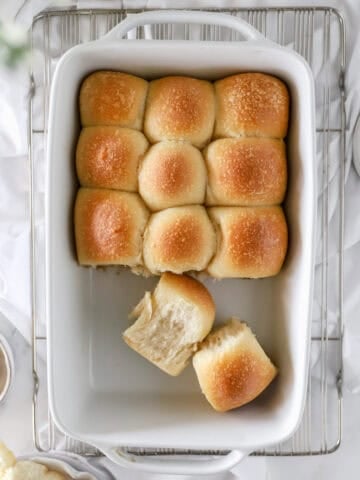 A top view of a white baking dish filled with golden sourdough dinner rolls.
