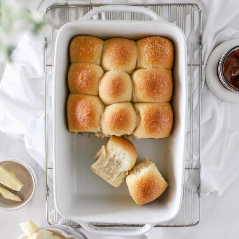 A top view of a white baking dish filled with golden sourdough dinner rolls.