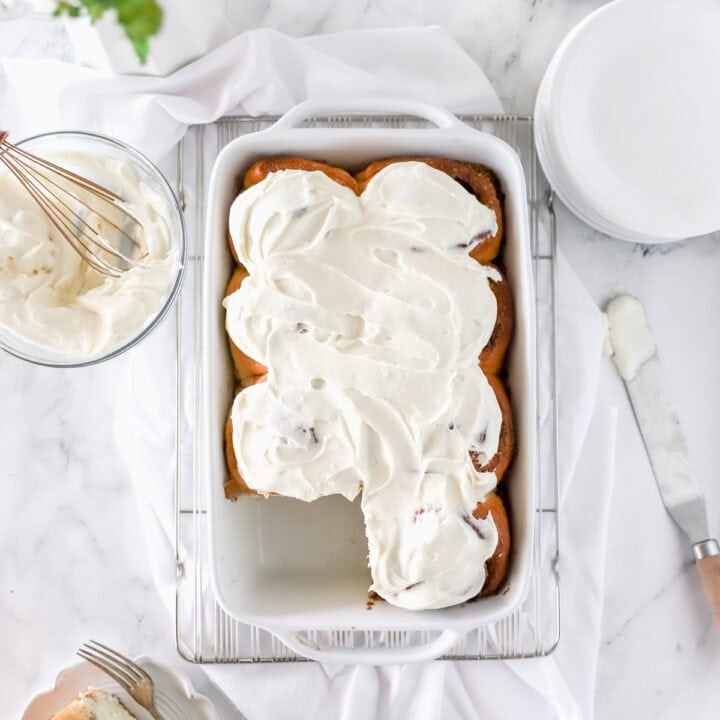 A top view of a white baking dish with sourdough cinnamon rolls with cream cheese frosting.