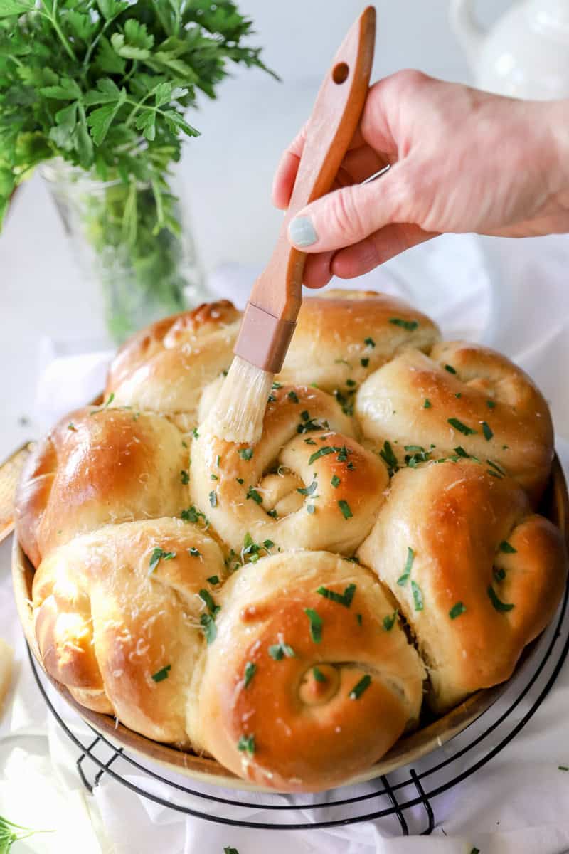 Step 8 of baking sourdough garlic knots is brushing with garlic butter, sprinkling with fresh parmesan.