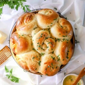 A close up view of the top of a round baking dish filled with sourdough garlic knots and grated parmesan.
