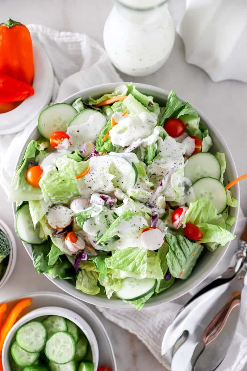 A top view of a mixed green salad with tomatoes and cucumbers topped with homemade ranch salad dressing.
