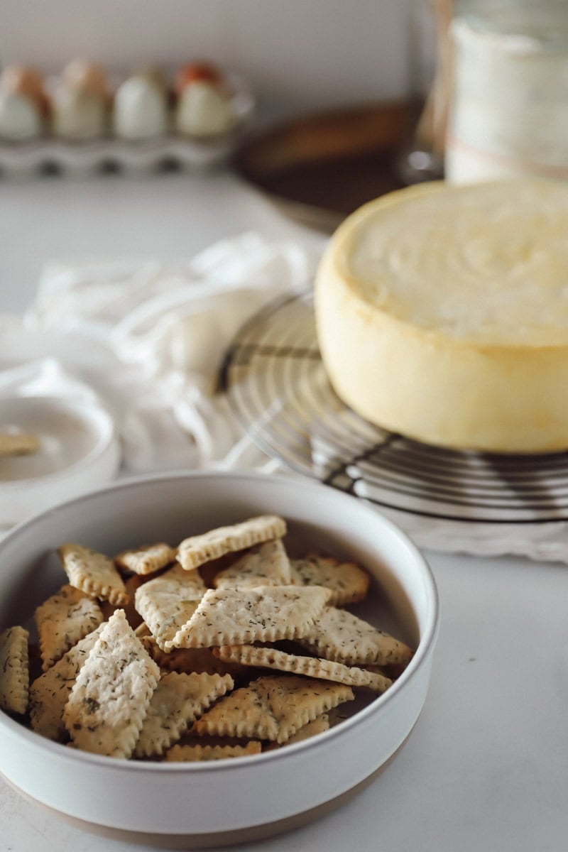 Serving suggestion for sourdough discard ranch crackers is to serve with cheese, showing a large wheel of gouda cheese.