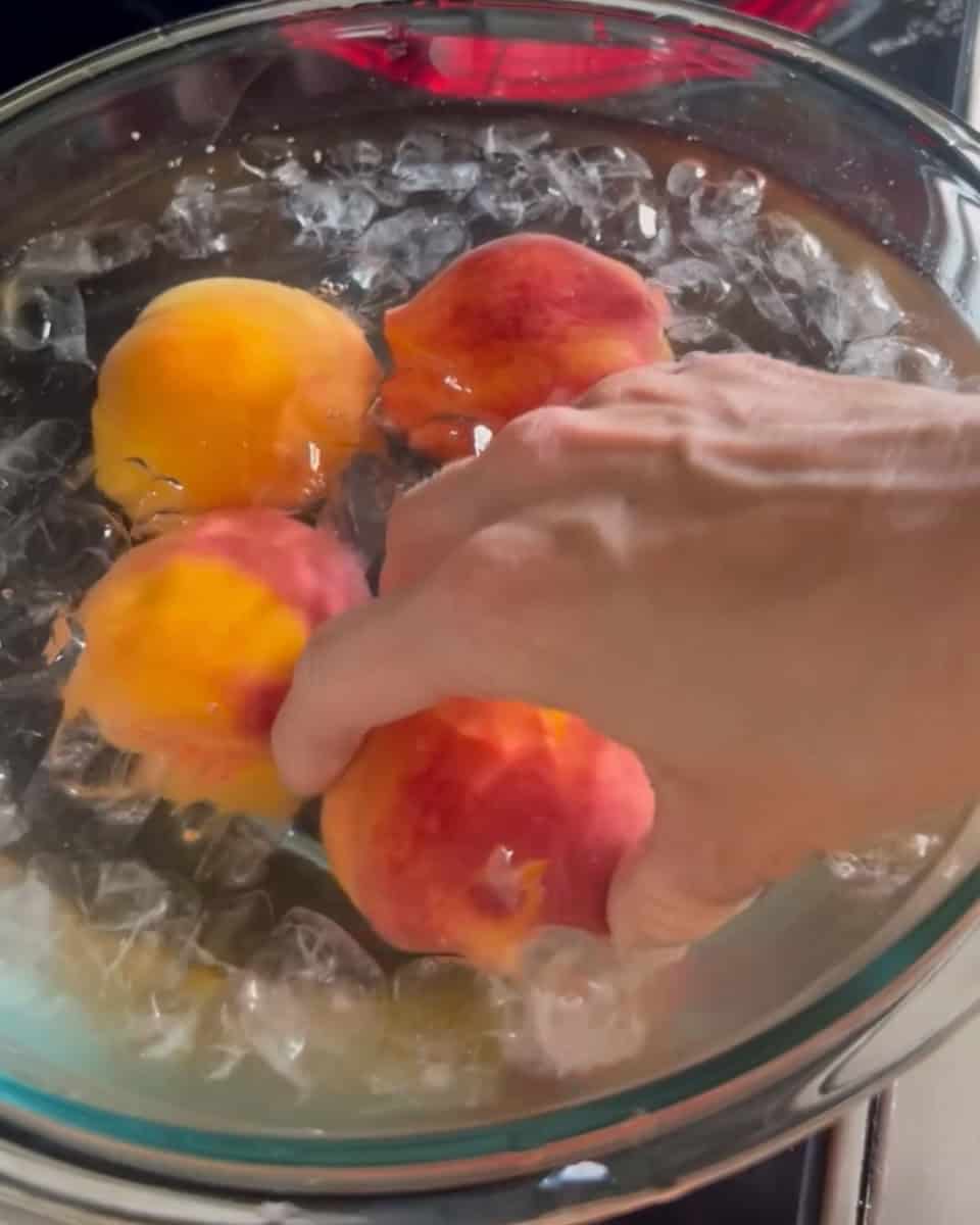 Step 2 of canning peaches is transferring the blanched peaches to a bowl of ice water with lemon.