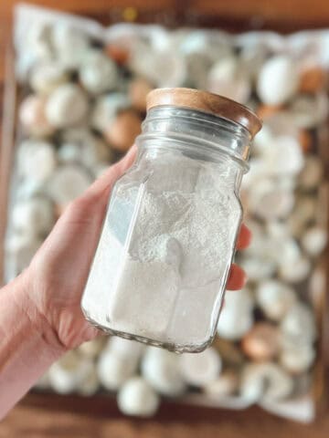 A hand holding a jar of egg shells that are ground into powder to show how to compost egg shells for plants.