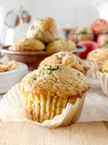 A close up view of a sourdough apple zucchini muffin with the wrapper slightly unwrapped to show the detailed crumb.