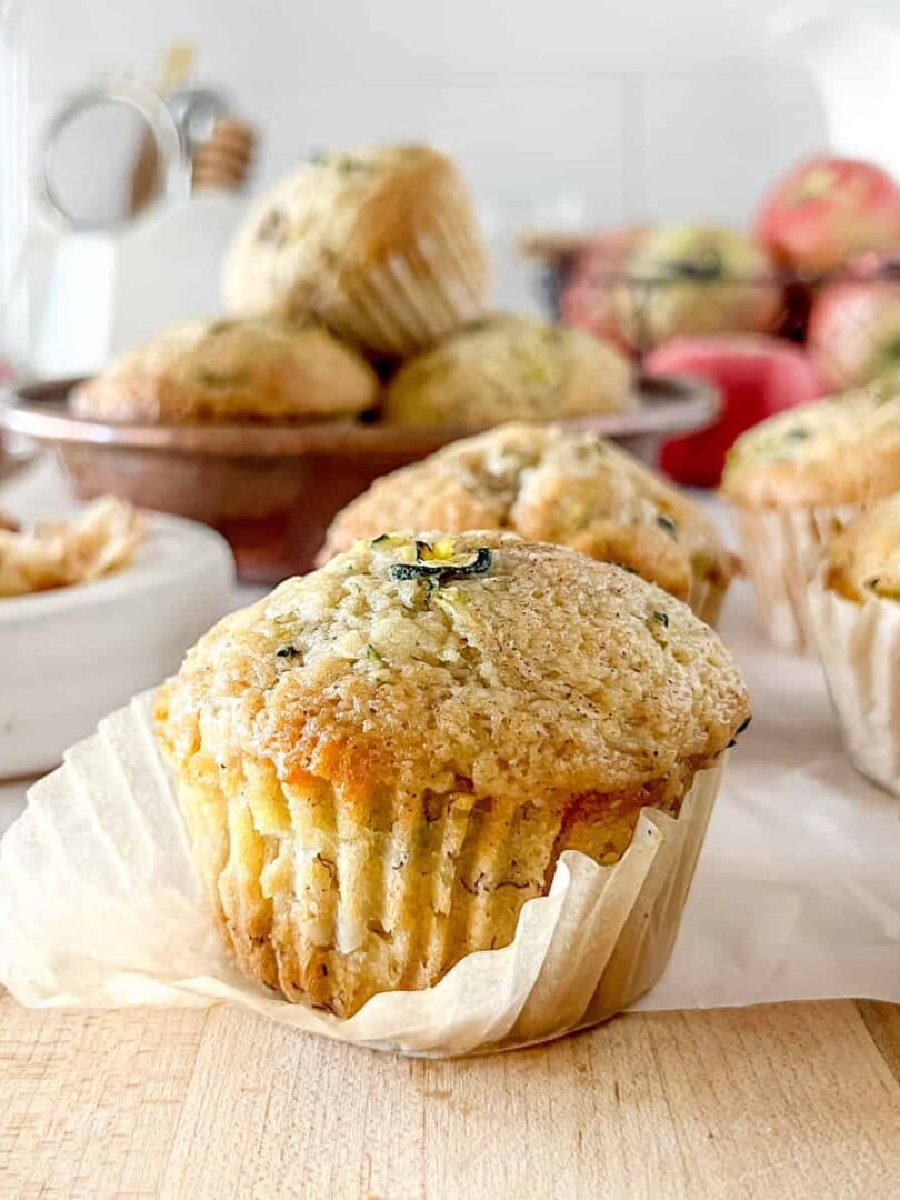A close up view of a sourdough apple zucchini muffin with the wrapper slightly unwrapped to show the detailed crumb.