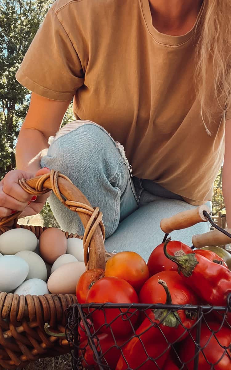 Meg holding a basket of tomatoes and a wicker basket filled with eggs.