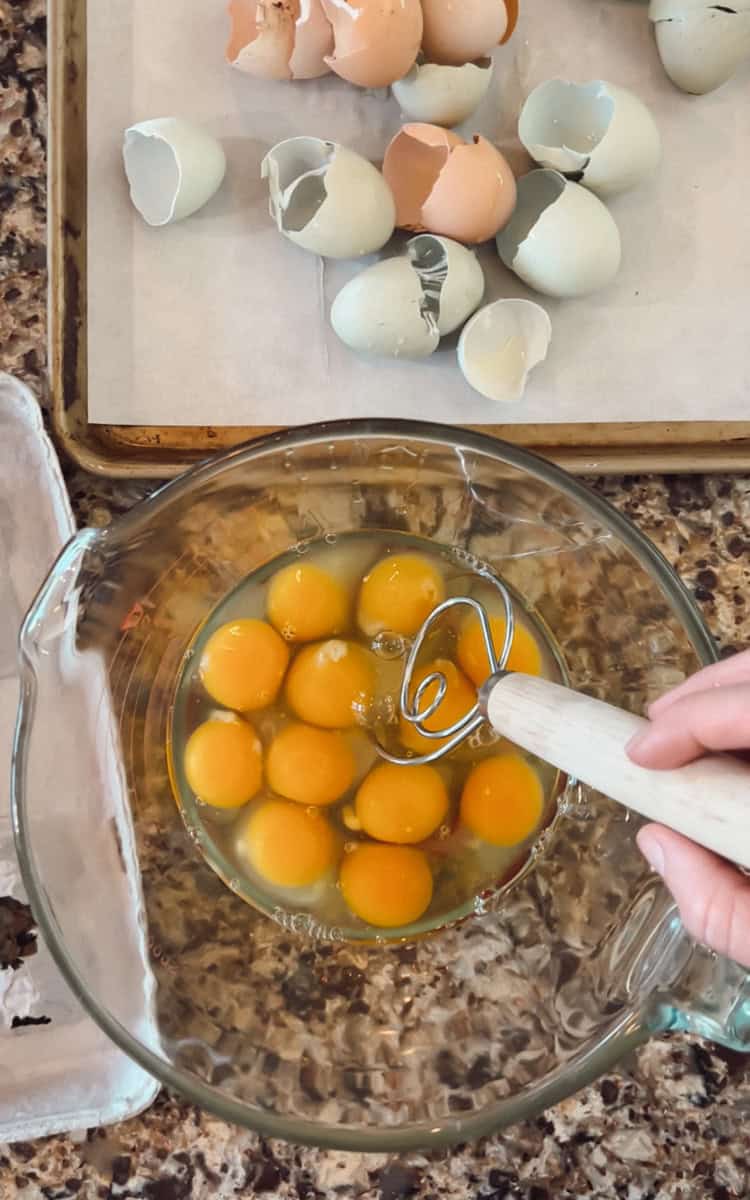 Eggs cracked into a bowl with the eggs shells piled on a cookie sheet.
