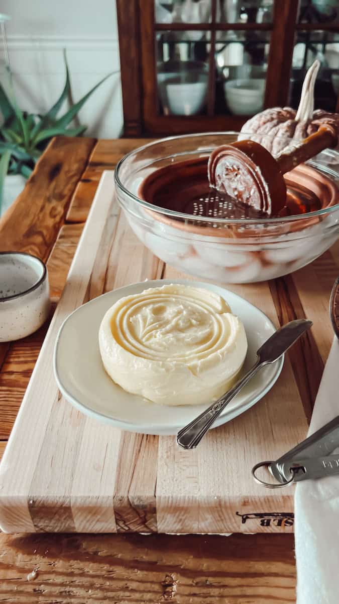 A wood cutting board layered with a bowl of ice water, antique butter press and molds, and fresh butter stamped with a lovely floral pattern.