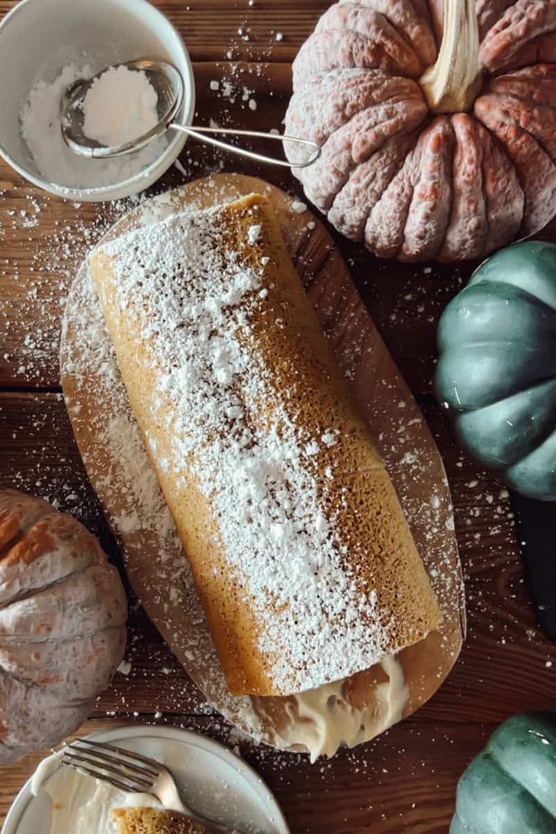 A top view of a sourdough pumpkin roll dusted with powdered sugar and surrounded by pie pumpkins.