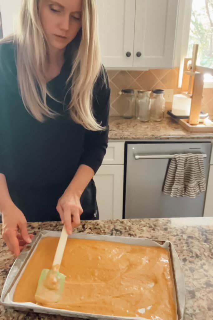 Step 4 of making a pumpkin roll is spreading the batter into a prepared baking sheet.