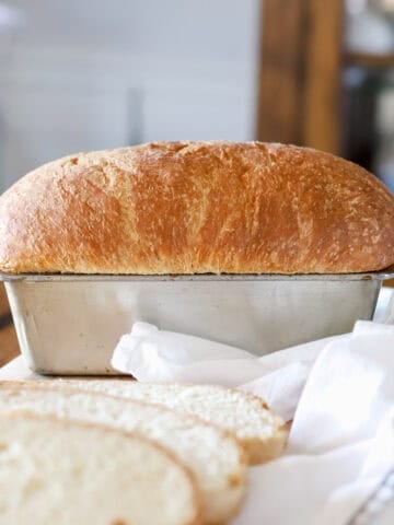 Homemade sandwich bread in a baking pan with slices around it.