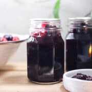 Two jars of whole berry cranberry sauce with a colander of fresh cranberries.