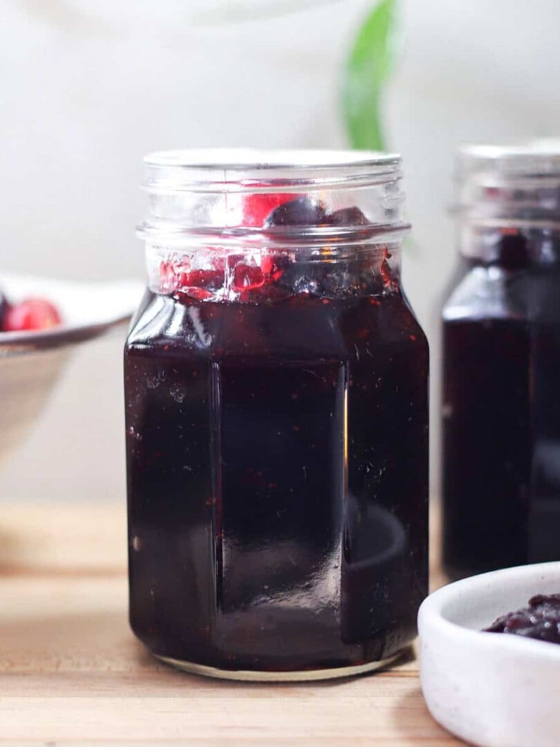 Two jars of whole berry cranberry sauce with a colander of fresh cranberries.