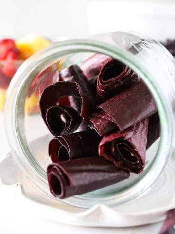Fruit leather rolled like fruit roll-ups in a glass jar up close showing detail.