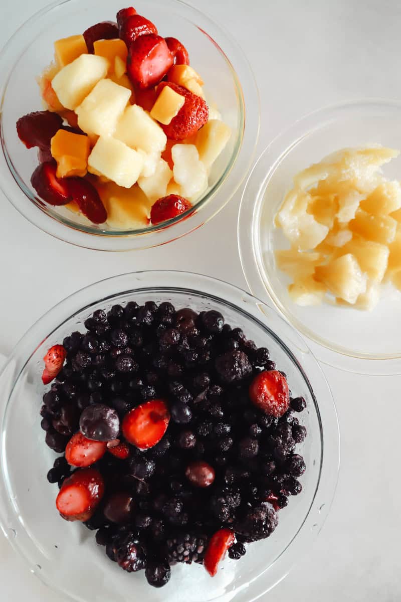 Ingredients for homemade fruit leather including frozen berries, pineapple and strawberries in glass prep bowls.