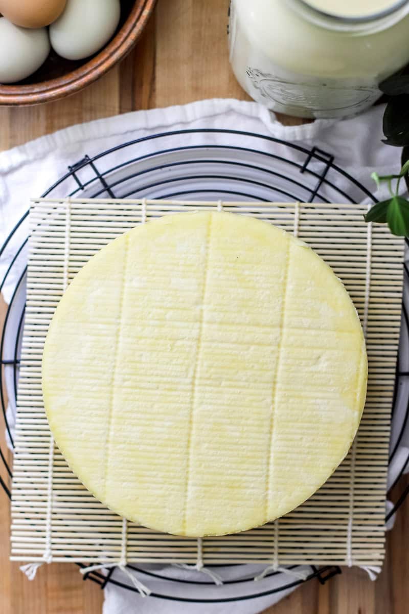 Top view of a wheel of white cheddar cheese drying on a bamboo mat.