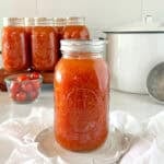A mason jar of canned tomatoes with a canner and other jars behind it.