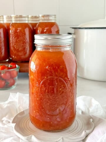 A mason jar of canned tomatoes with a canner and other jars behind it.