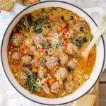 Overhead view of creamy meatball soup with pasta, meatballs, and spinach in a white pot.