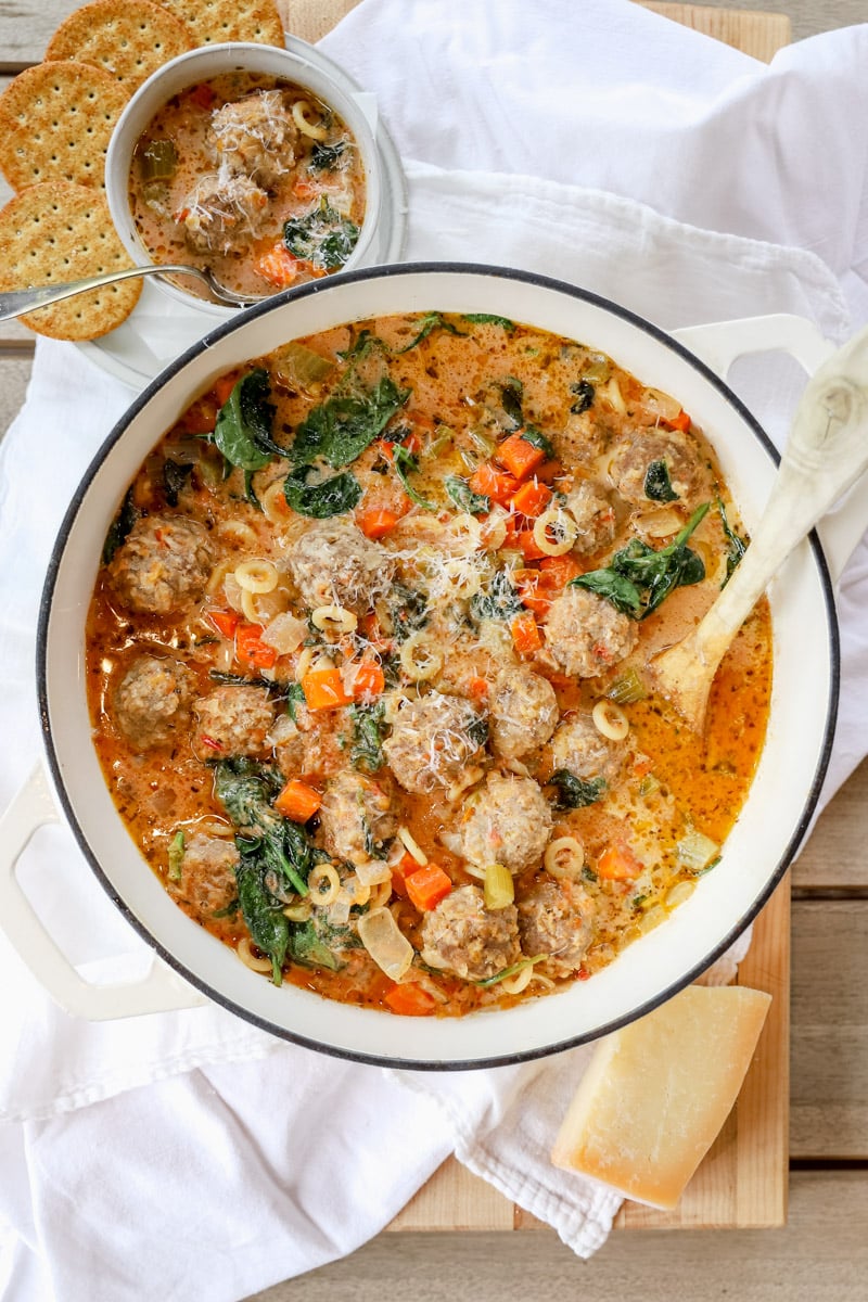 Creamy meatball soup in a white Dutch oven topped with freshly grated parmesan and spinach.