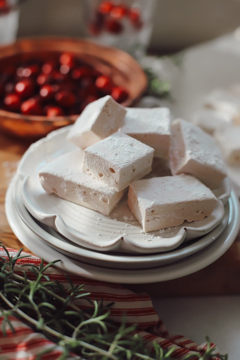 A plate of cranberry marshmallows stacked on top of each other with rosemary and cranberry garnishes.