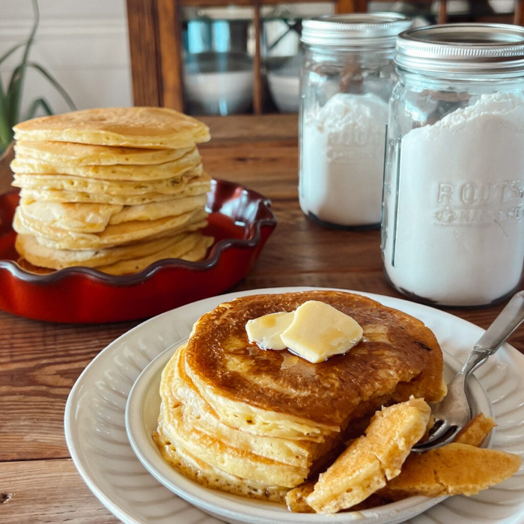 Homemade pancakes stacked on a plate with a jar of pantry pancake mix in the background.