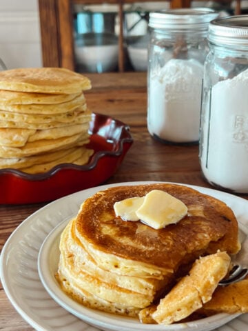 Homemade pancakes stacked on a plate with a jar of pantry pancake mix in the background.