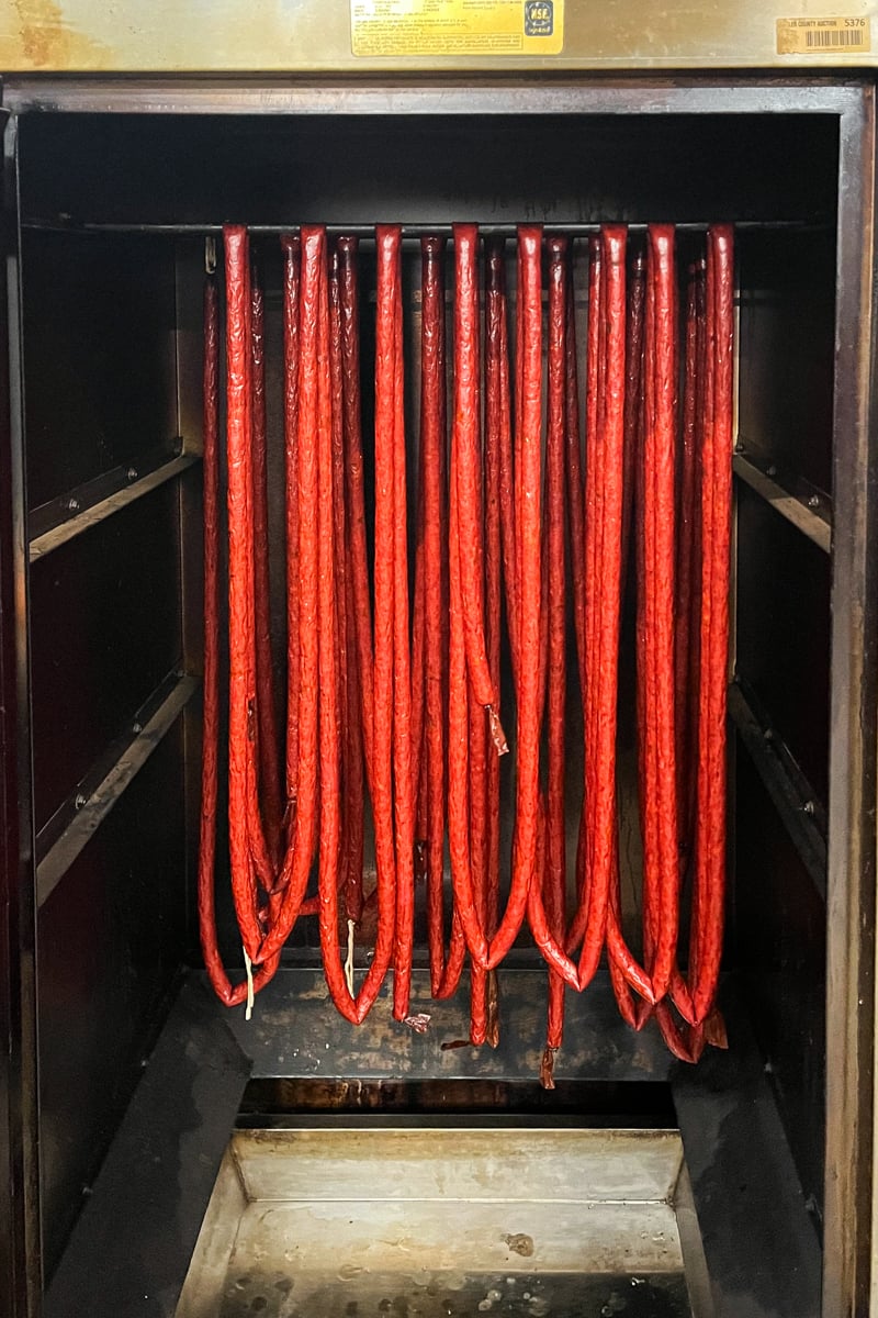Homemade jalapeño cheddar snack sticks hanging in a smoker.