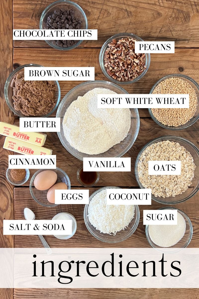 A top view of the ingredients for homemade cowboy cookies with fresh milled flour in prep bowls including chocolate chips, pecans, coconut, soft white wheat berries, and more.