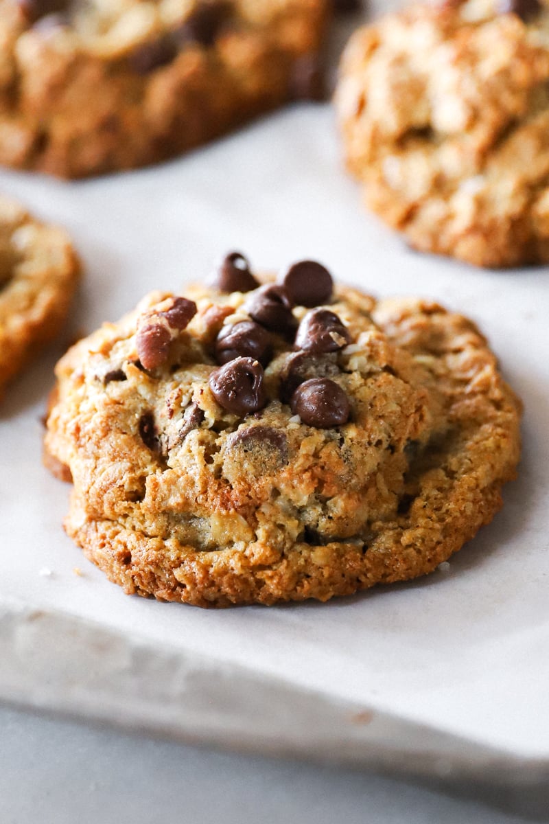 A side view of a Cowboy Cookies with Fresh Milled Flour on a parchment lined baking sheet showing detail of chocolate chips, coconut and pecans.