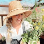 How to make money homesteading with a homesteader in a greenhouse wearing a sun hat holding a potted vegetable plant.