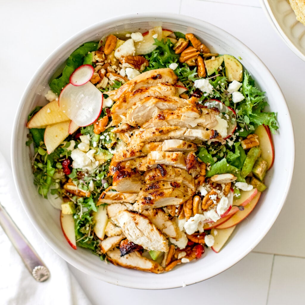 Harvest chicken salad topped with sliced chicken breast, apples, pecans, feta cheese, avocado, and radishes over mixed greens.