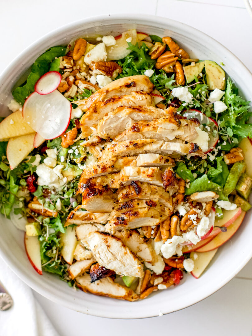 Harvest chicken salad topped with sliced chicken breast, apples, pecans, feta cheese, avocado, and radishes over mixed greens.