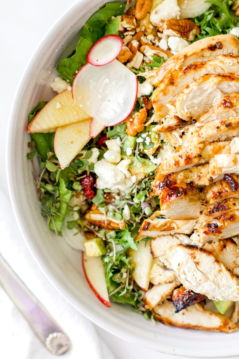 Close up of harvest chicken salad with sliced chicken breast, apples, radishes, feta cheese, pecans, avocado, and microgreens.