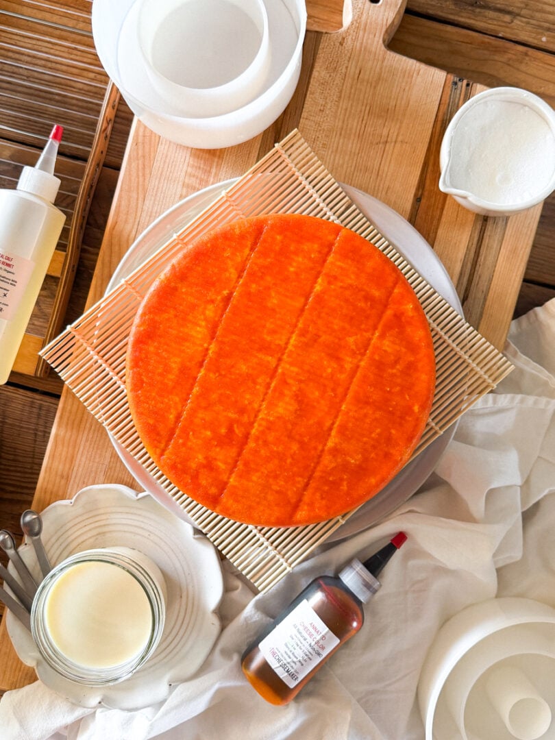 Beginner cheesemaking equipment including a homemade Colby cheese wheel, rennet, annatto, cheese molds, cultures, and curd cutting tools.