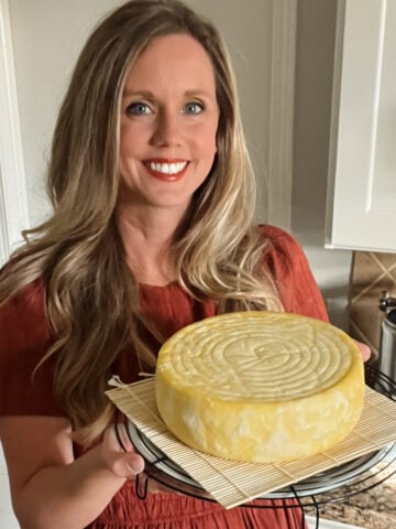 Meg holding homemade Gouda cheese wheel held in kitchen after pressing, made from fresh milk using traditional method.