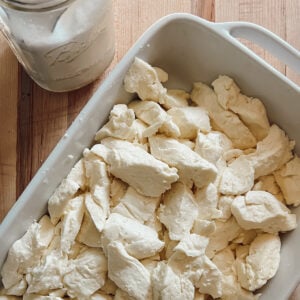 Fresh homemade cheddar cheese curds in a white baking dish on a wooden cutting board.