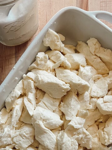 Fresh homemade cheddar cheese curds in a white baking dish on a wooden cutting board.