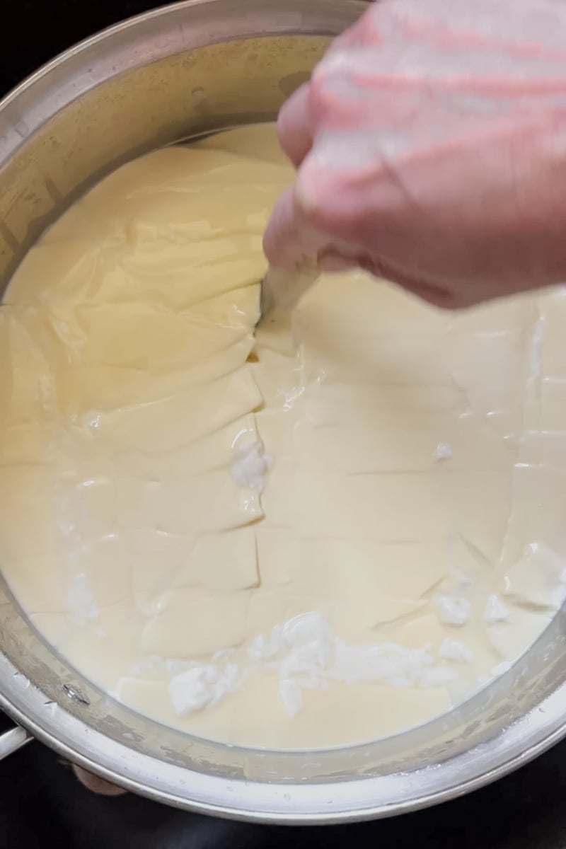 Cutting homemade cheddar cheese curds into ½-inch cubes with a long knife.